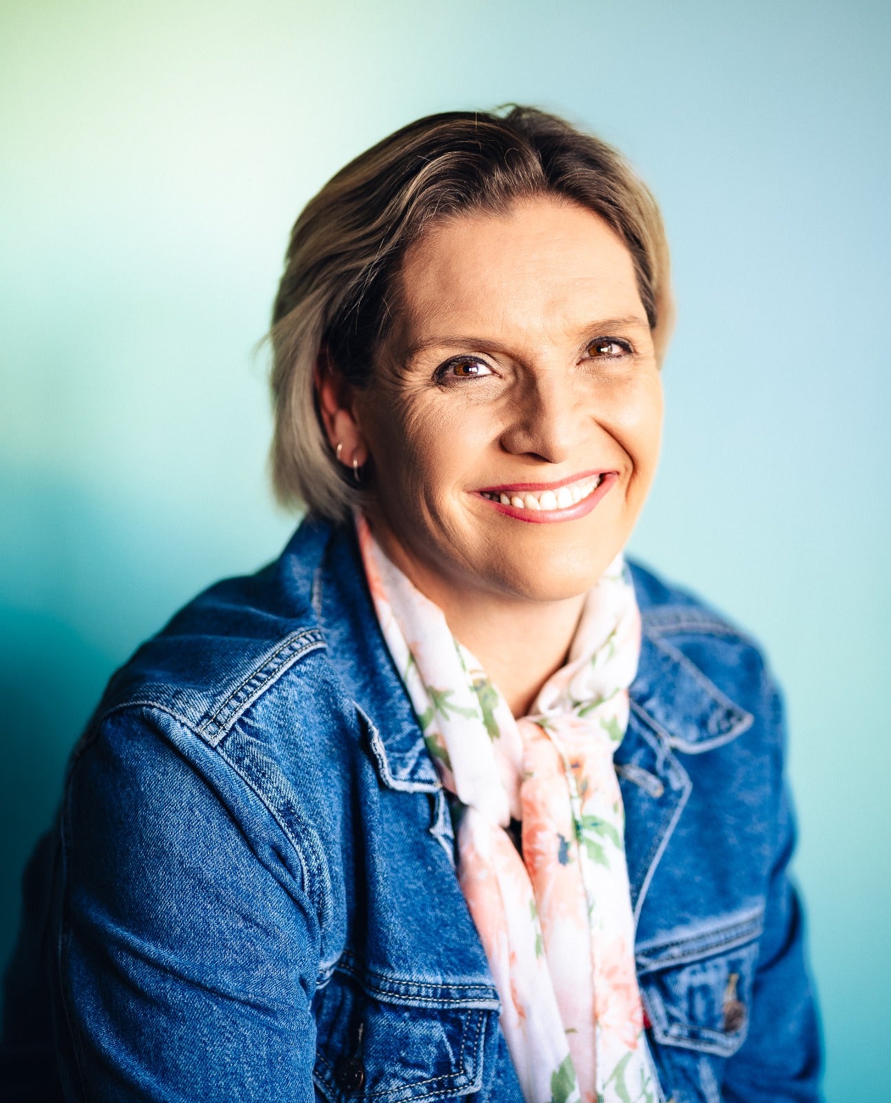 Woman wearing a denim jacket and floral scarf against a light blue background