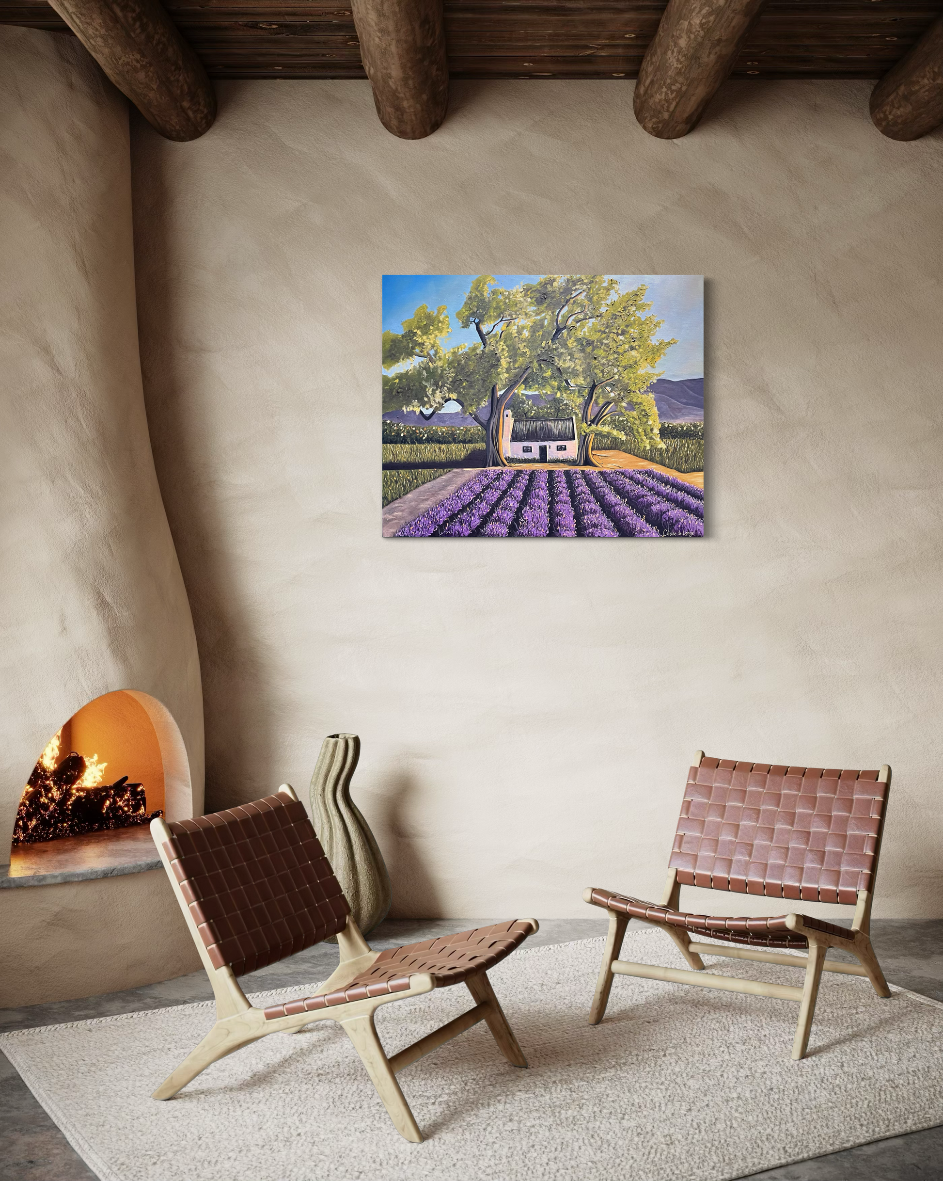 Two woven chairs in a room with a fireplace and a painting of a house with lavender fields on the wall.