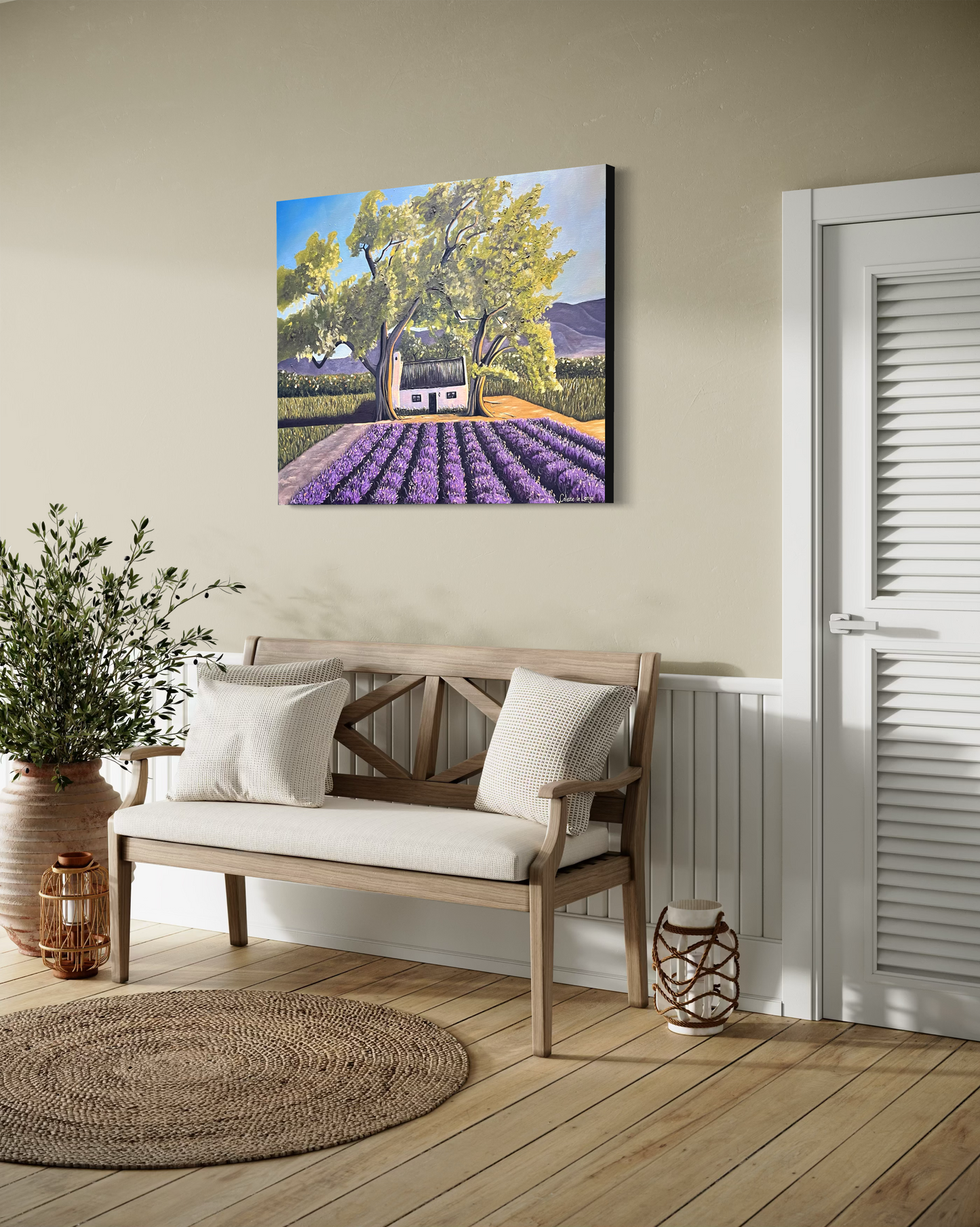 Lavender field painting on a wall above a wooden bench with cushions.